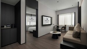 Une chambre d’hôtel moderne, équipée d’un lit, d’un canapé, d’une table basse et d’un bureau avec un ordinateur. Deux panneaux encadrés sont accrochés au mur, l’un au-dessus du lit et l’autre au-dessus du bureau.