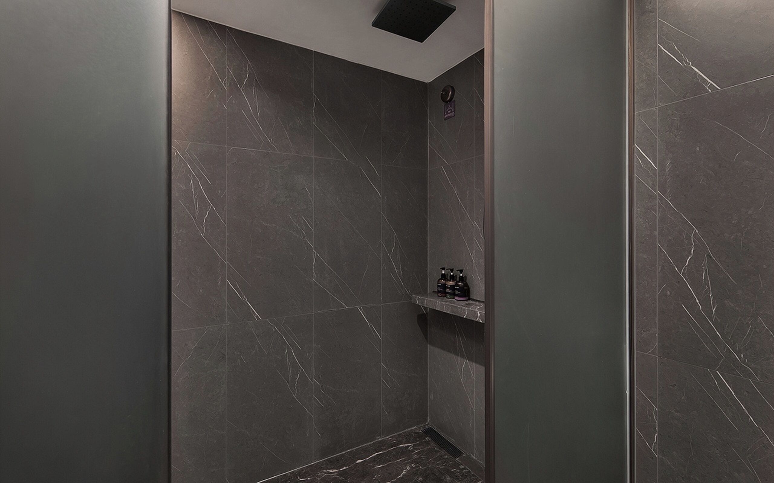 Une douche moderne avec des murs en marbre foncé et une étagère contenant des articles de toilette.