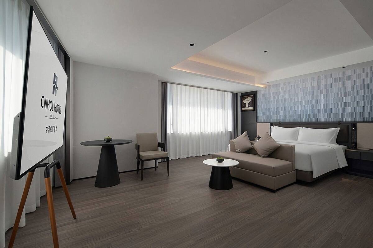 Une chambre d’hôtel moderne, équipée d’un lit, d’un canapé, de deux fauteuils, d’une petite table et d’une grande fenêtre avec des rideaux.