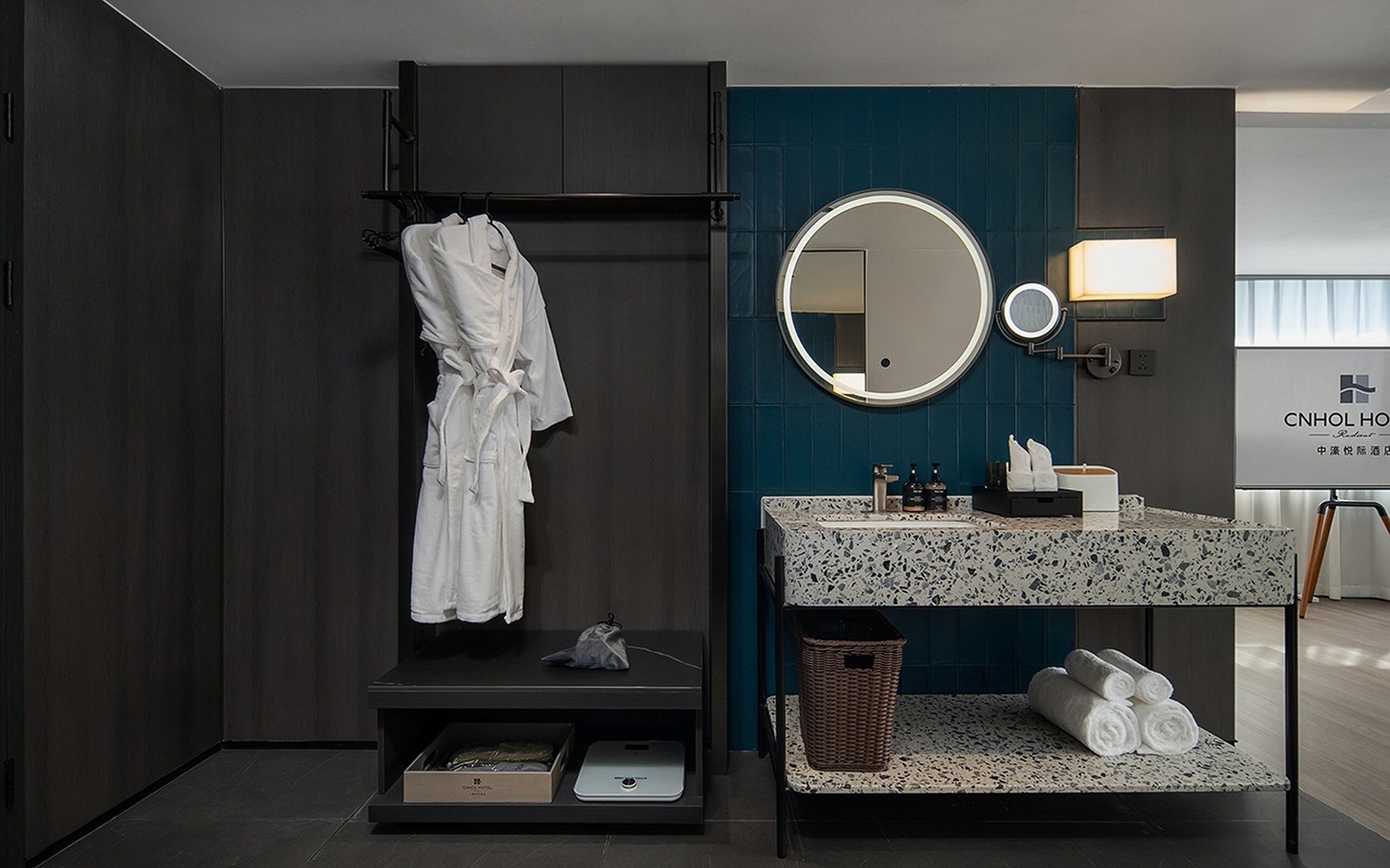 Een moderne badkamer met een donker houten wastafelmeubel, een ronde spiegel en een badjas aan een rek.