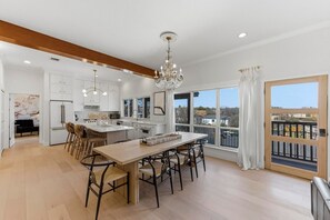A modern kitchen with white cabinetry, a central island, and a dining area with bar stools. - Modern Zilker Retreat | Downtown Views + Walk to ACL & Barton Springs (Austin)