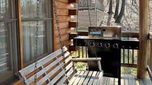 A wooden cabin with a swing chair, a grill, and a view of trees. - The Hawthorn on Table Rock Lake, 2 Bed/2 Bath Log Cabin, Pool, Hot Tub & Dock (Shell Knob)