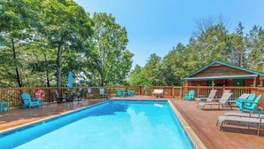 A rectangular swimming pool with a wooden deck surrounding it, equipped with lounge chairs and a small cabin in the background. - The Hawthorn on Table Rock Lake, 2 Bed/2 Bath Log Cabin, Pool, Hot Tub & Dock (Shell Knob)