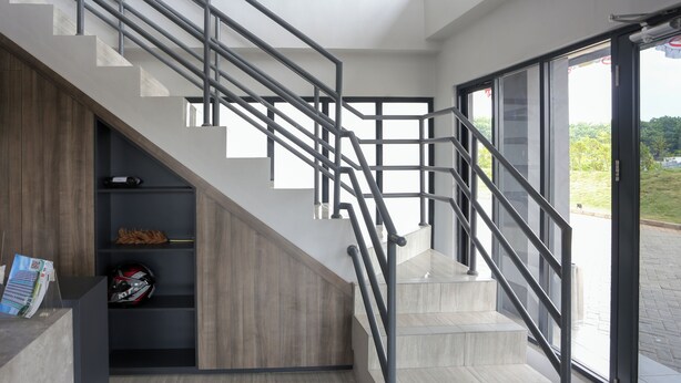Un escalier moderne avec des rampes en métal, une étagère en bois avec divers objets, et une vue à travers une porte vitrée.