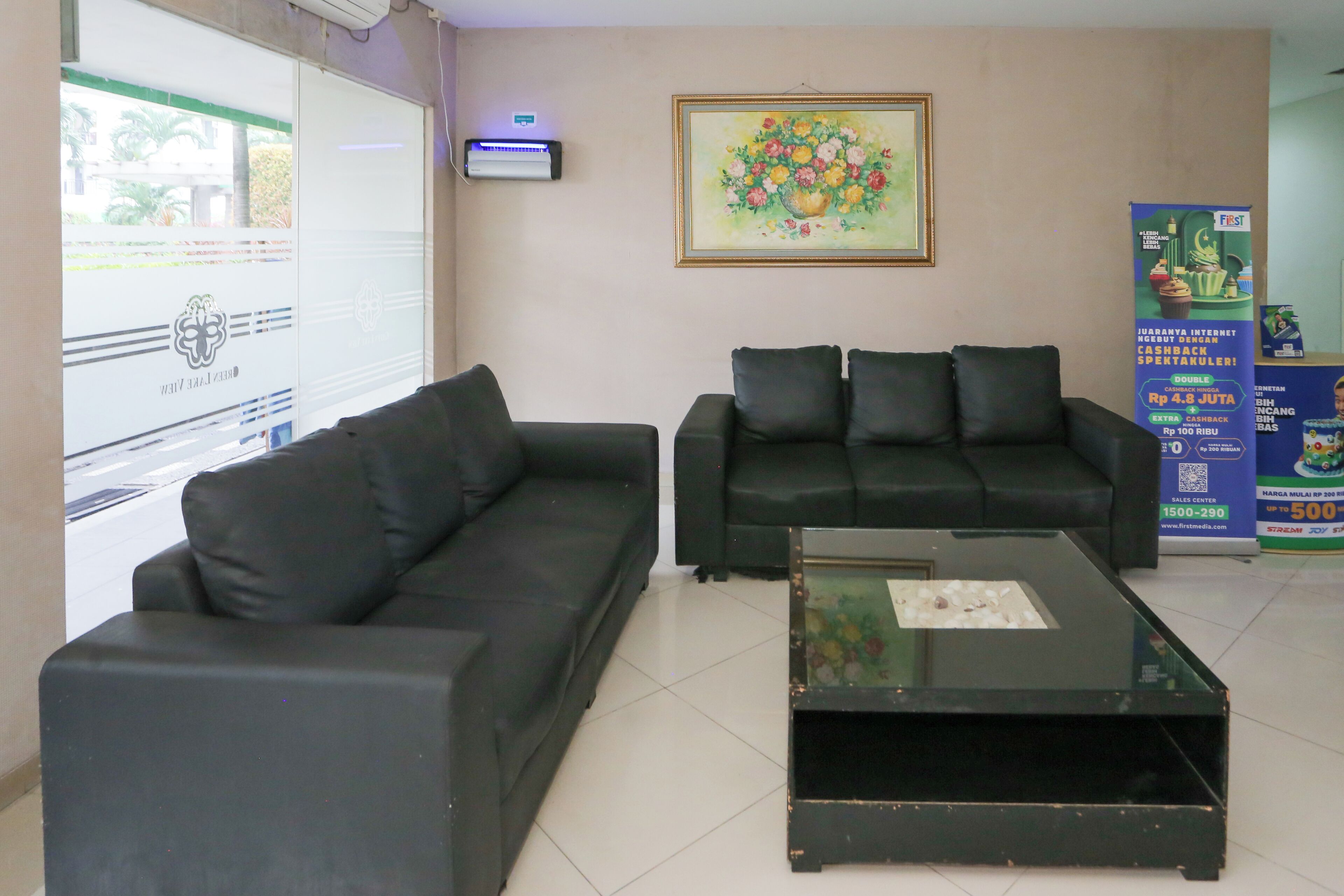 Un área de recepción con dos sofás negros, una mesa de centro de vidrio y un cuadro floral en la pared.