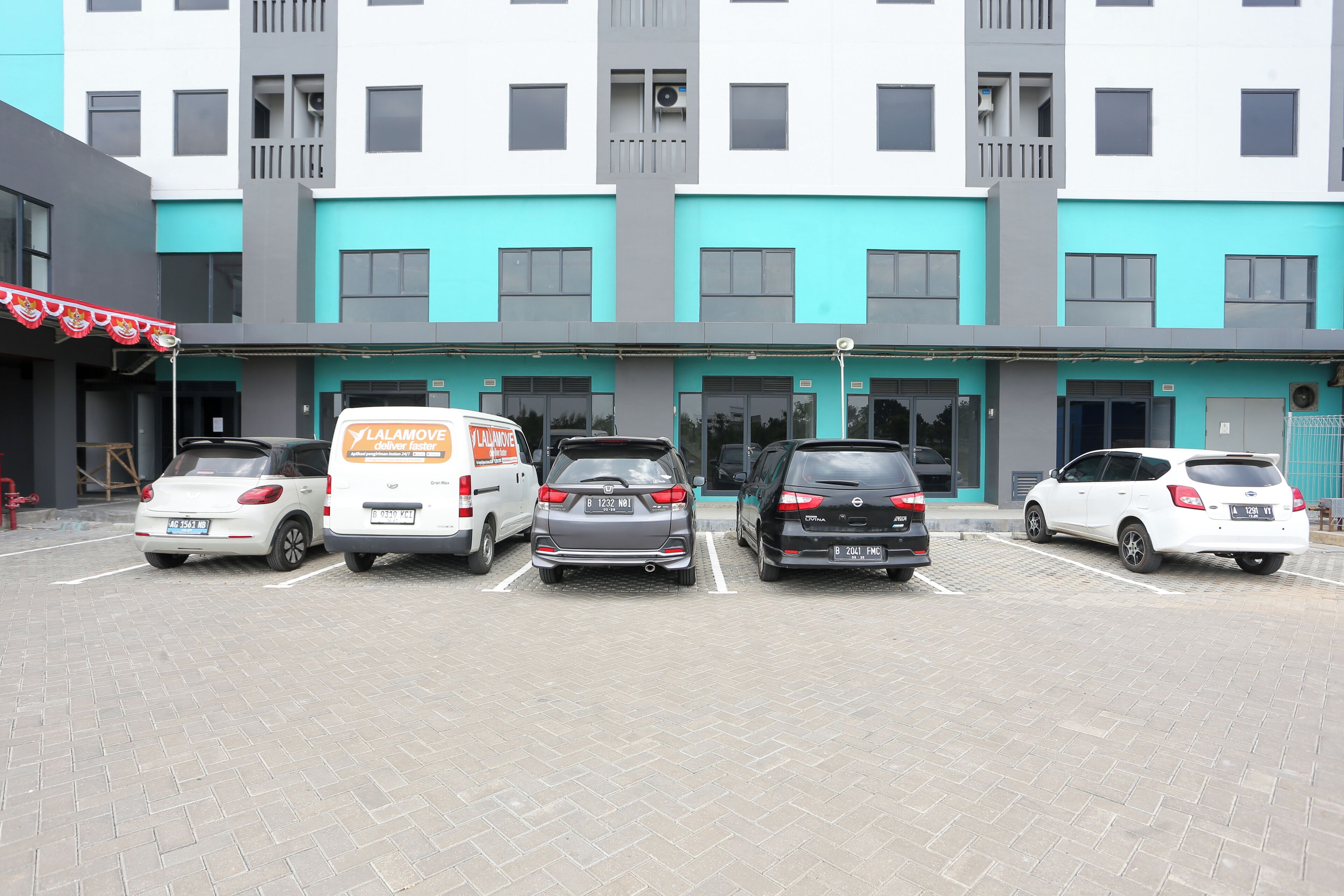 Een parkeerplaats met vijf auto's en een verhuiswagen voor een gebouw met turquoise en grijze gevels.