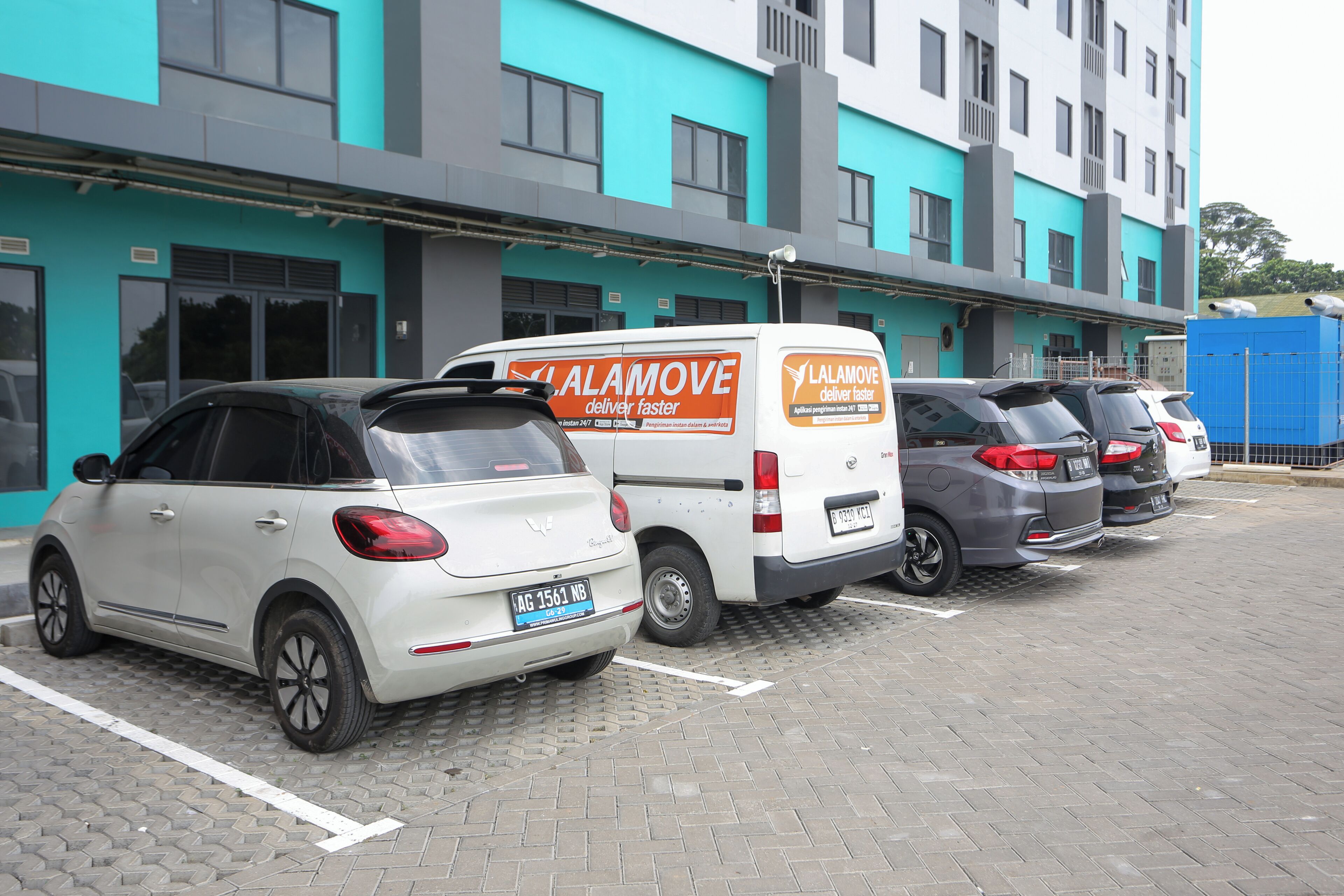 Un parking avec plusieurs voitures et un fourgon blanc arborant le logo « Lalamove ».