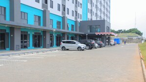 Un espace de stationnement avec plusieurs voitures, un bâtiment à la façade bleue et grise, et une personne qui marche au loin.