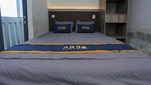 Une chambre d’hôtel avec un lit agrémenté d’une couvre-lit grise et bleue ornée du logo « ARBA Hospitality ».