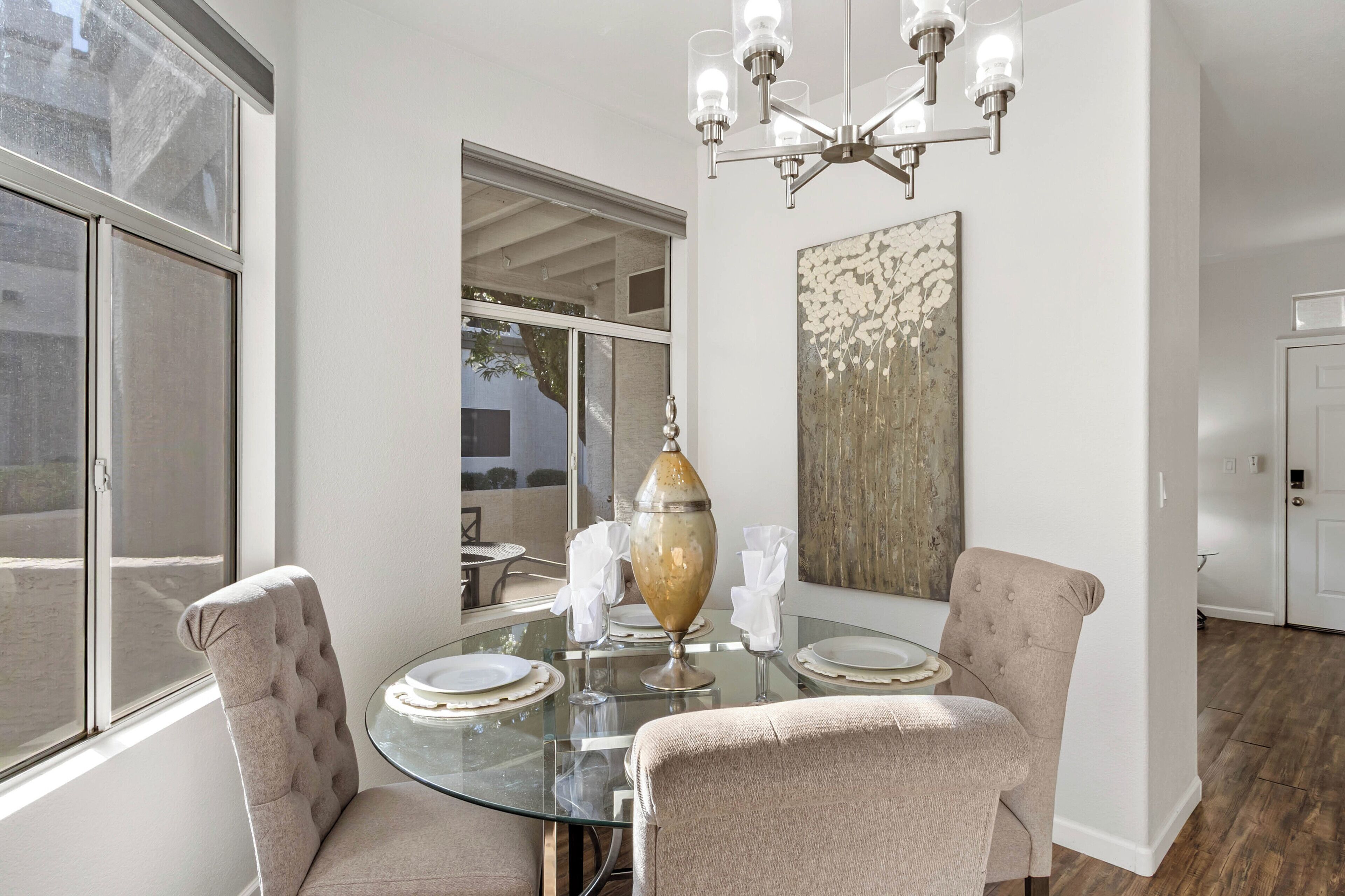 A dining area with a glass table, two upholstered chairs, a chandelier, and a large vase.