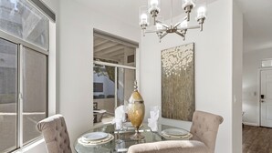 Zona pranzo con tavolo in vetro, due sedie imbottite, un lampadario e un vaso grande.