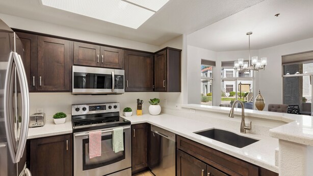 Una cucina moderna con mobili in legno scuro, elettrodomestici in acciaio inossidabile e un'ampia finestra che si affaccia su una zona residenziale.