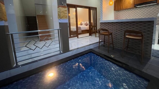 A modern indoor pool area with a glass barrier, wooden chairs, and a visible bedroom in the background. - Desta House Ubud (Ubud)