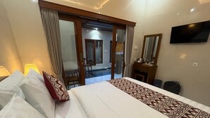 A hotel room with a large bed, a desk, a chair, a TV, and a sliding glass door leading to a balcony. - Desta House Ubud (Ubud)