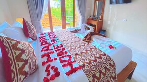 A hotel room with a bed, a TV, and a balcony with curtains. - Desta House Ubud (Ubud)