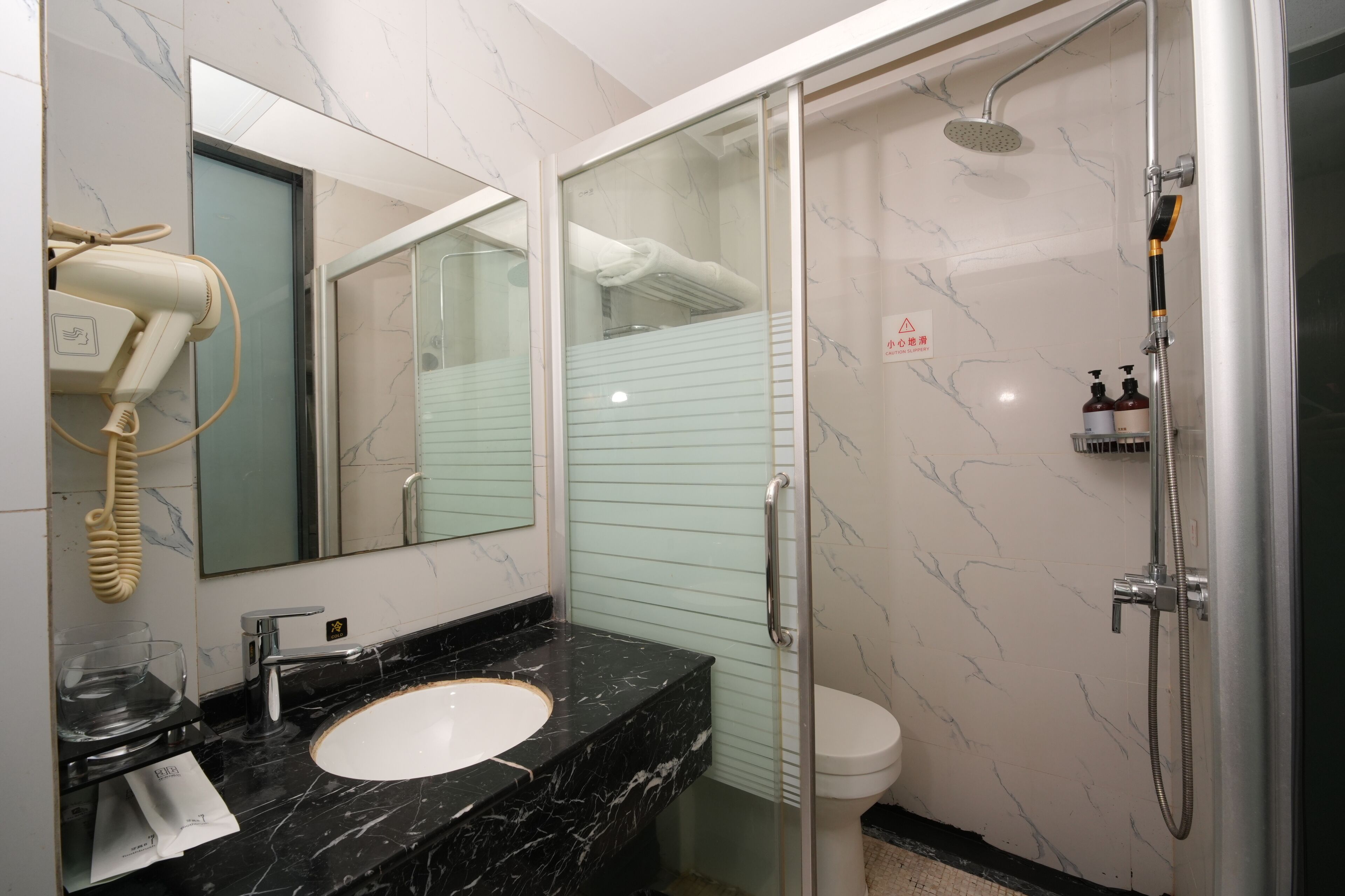 A bathroom with a marble sink, a glass-enclosed shower, a hairdryer, and a toilet.