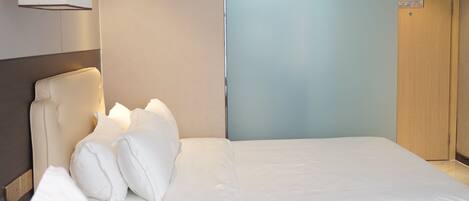 A hotel room with a bed, a headboard, a wall-mounted lamp, and a door.