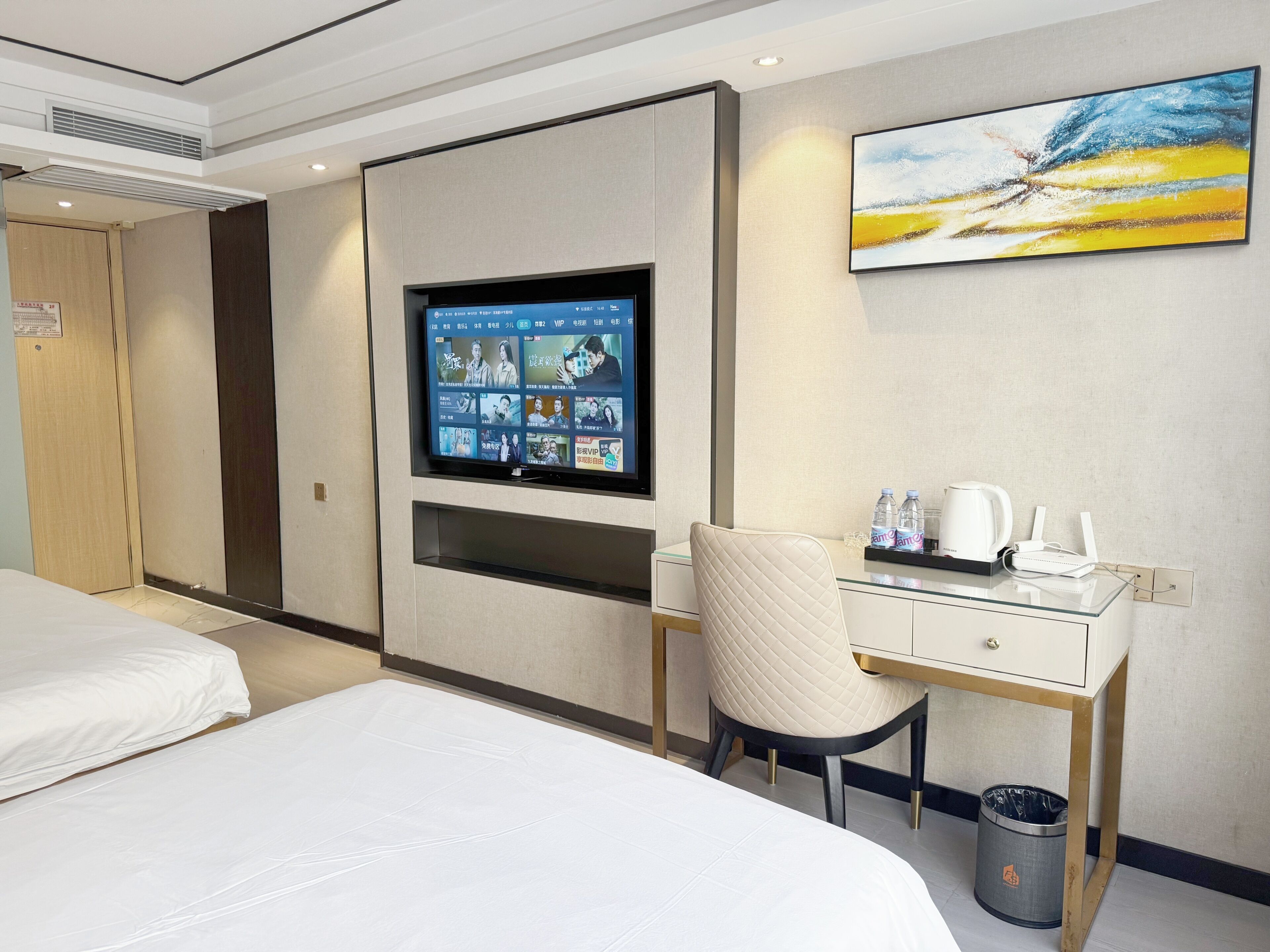 A hotel room with a bed, a desk with a chair, a television, and a painting on the wall.