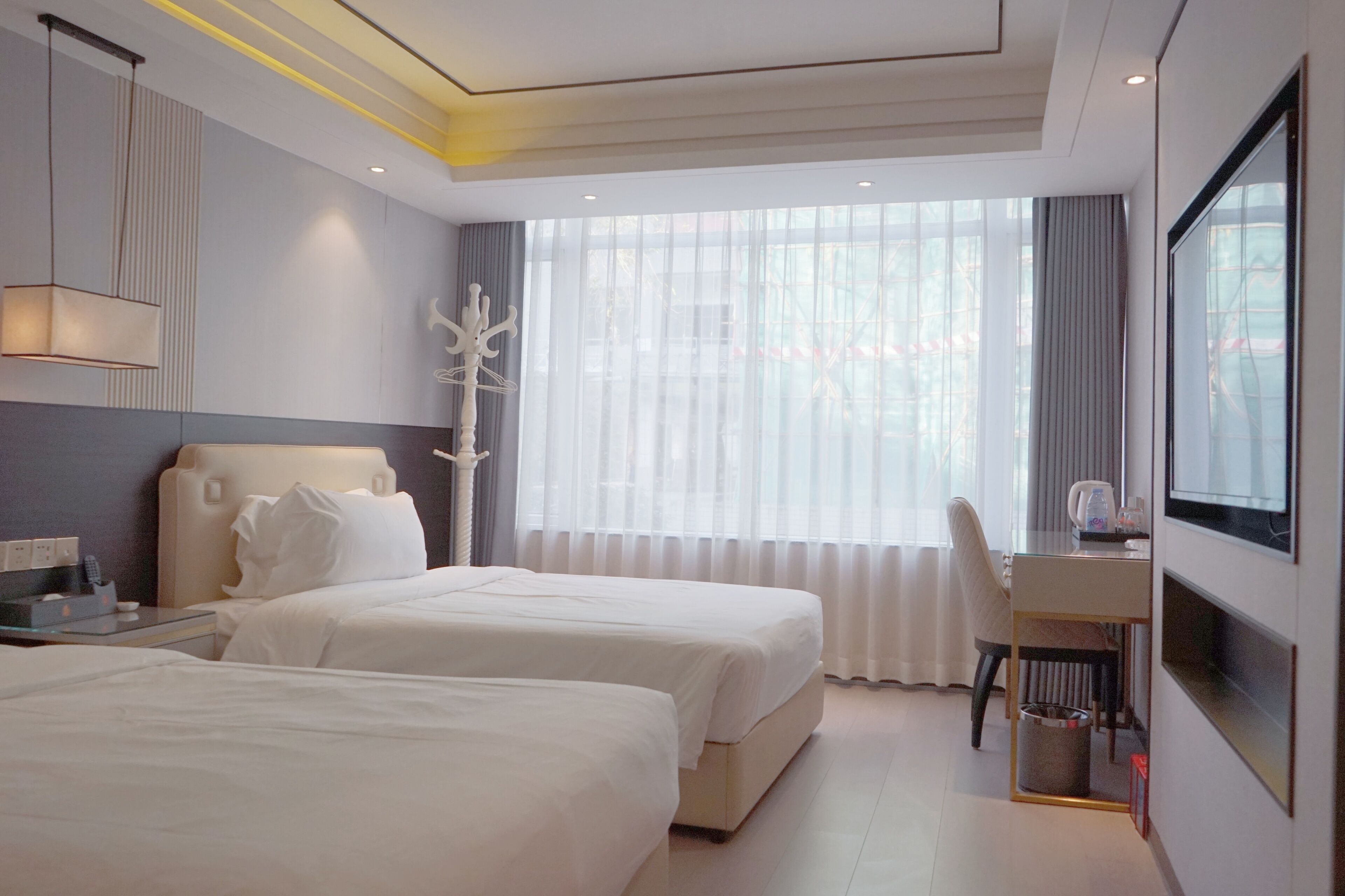 A hotel room with two beds, a desk, a chair, and a large window with curtains.