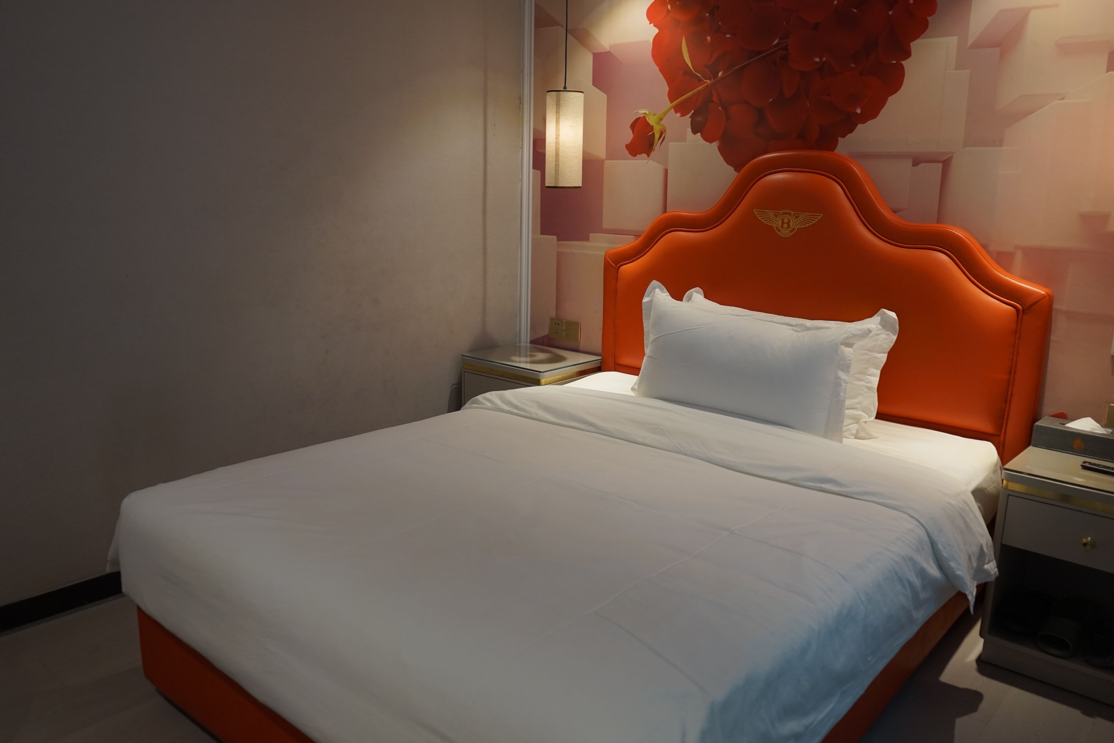 A bed with an orange headboard, white bedding, and a nightstand with a lamp.