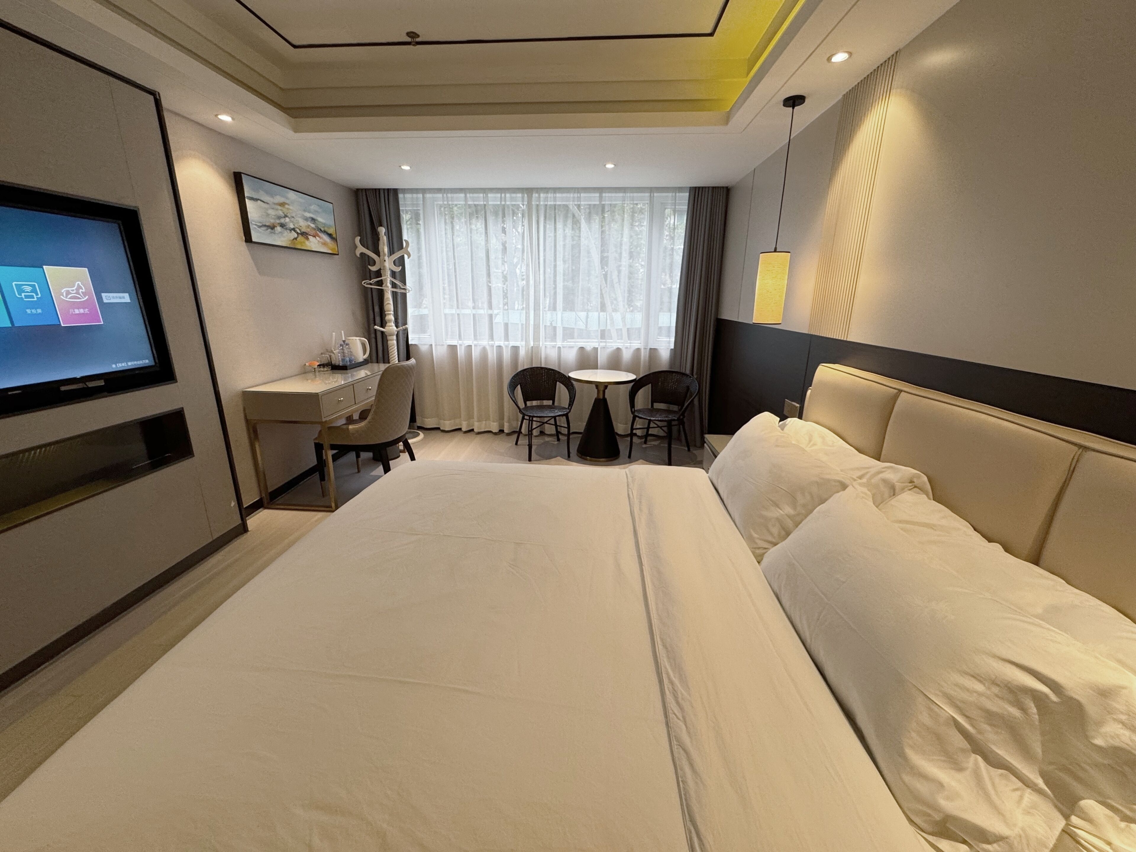 A hotel room with a large bed, a desk with a chair, a television, and a window with curtains.
