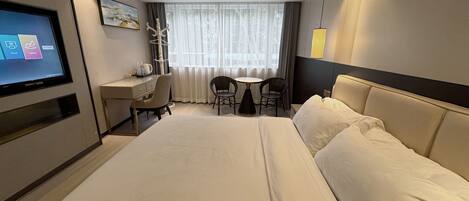 A hotel room with a large bed, a desk with a chair, a television, and a window with curtains.