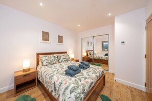 A bedroom with a large bed, wooden nightstands, a mirror, and a door. - The Steading Family Friendly Getaway (Peterhead)