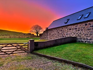 A stone building with a sloped roof, a wooden gate, and a grassy area in front. - The Steading Family Friendly Getaway (Peterhead)