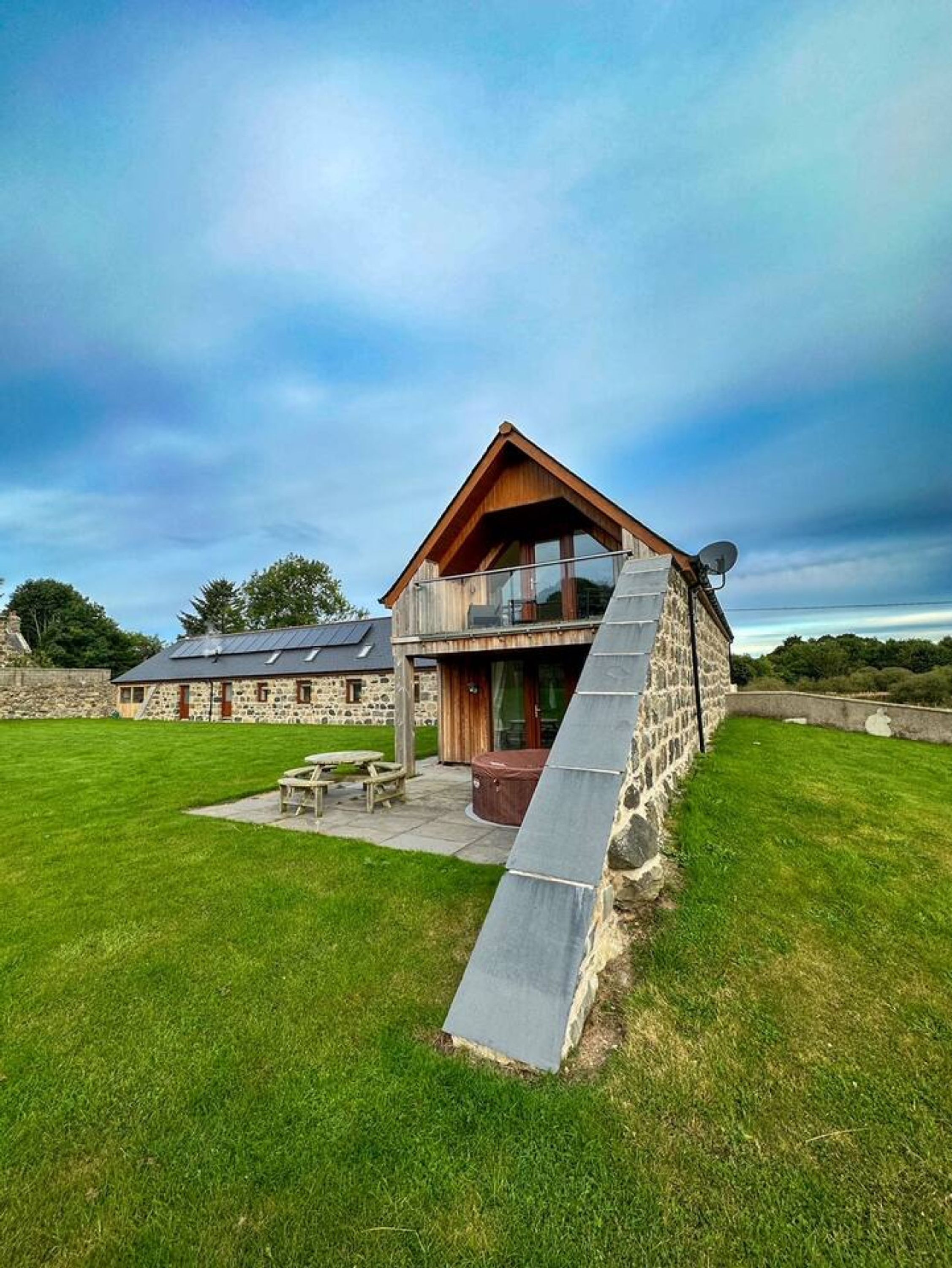 A modern house with a stone exterior, a wooden deck, and a large patio area.