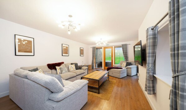 A modern living room with a grey sofa, a coffee table, and a TV mounted on the wall. - The Steading Family Friendly Getaway (Peterhead)