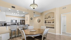 A kitchen with white cabinets, a microwave, and a refrigerator. There is a dining table with four chairs. - Welcome to Oceanwalk 15-505! (New Smyrna Beach)