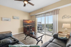 A living room with a sofa, a coffee table, a TV, and a balcony with a view. - Welcome to Oceanwalk 15-505! (New Smyrna Beach)