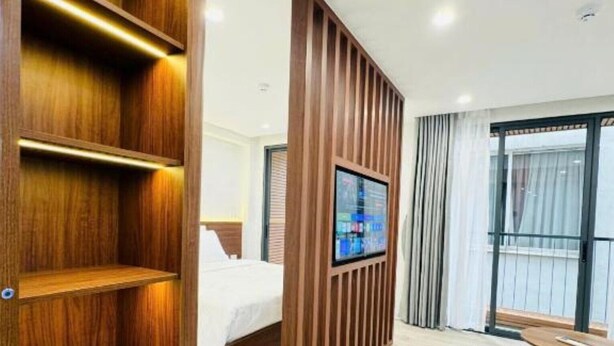 Ein modernes Hotelzimmer mit einer Holztrennwand, einem Bett, einem an einer Holzplatte montierten Fernseher und einem Balkon mit Blick.