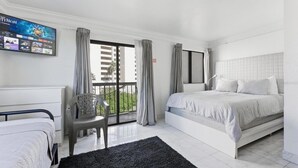 A hotel room with a bed, a desk, a chair, a TV, and a balcony with curtains.