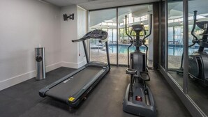 A gym with a treadmill and an elliptical machine, large windows, and a water feature outside.