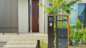Ein moderner Hauseingang mit Holztür, Briefkasten aus Metall und einem kleinen Garten mit Pflanzen.