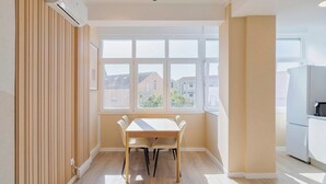 Una cuina moderna amb electrodomèstics blancs, una zona de menjador amb taula i cadires de fusta, i una finestra gran amb vista a edificis.