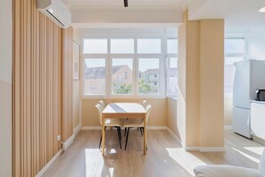A modern kitchen with white appliances, a dining area with a wooden table and chairs, and a large window with a view of buildings. - The Anna Apartment - Setúbal Central Station (Setúbal)