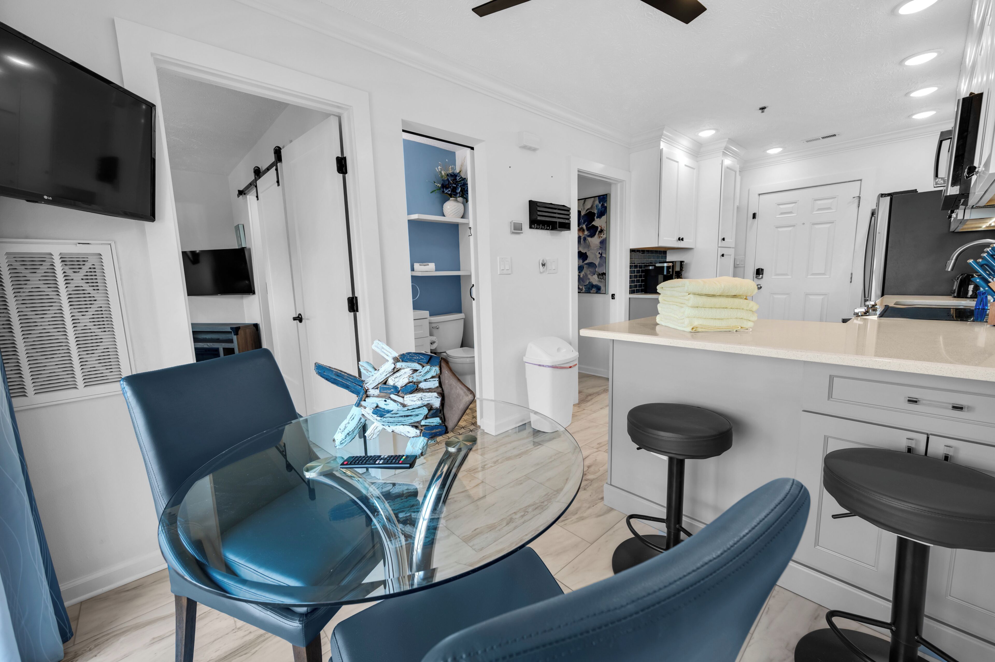 A modern kitchen with white cabinets, a black refrigerator, and a glass island with bar stools.