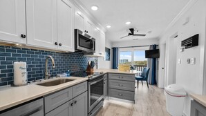 Una cocina moderna con armarios grises, salpicadero de azulejos azules, electrodomésticos de acero inoxidable y un comedor con vistas.