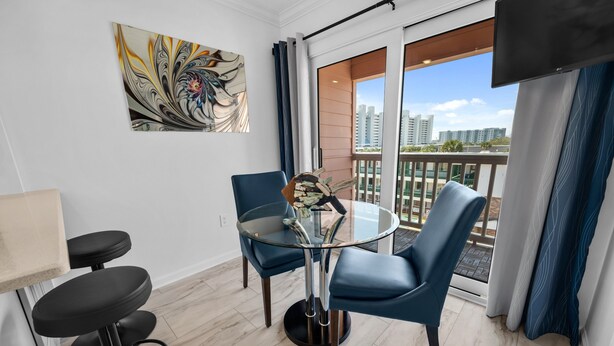 Una habitación moderna con una mesa de vidrio, sillas azules, un jarrón decorativo y vistas a la ciudad a través de grandes ventanales.