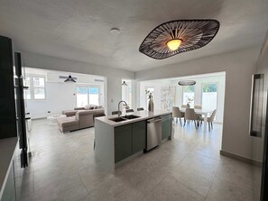 Eine moderne Küche mit einer zentralen Kochinsel, einem Essbereich mit Tisch und Stühlen sowie einem Wohnbereich mit Sofa und Couchtisch.