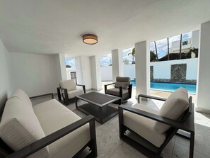 Ein modernes Wohnzimmer mit Blick auf einen Pool, ausgestattet mit einer Couch, Sesseln und einem Couchtisch.