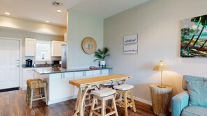 A modern kitchen with a central island, bar stools, a dining table, and a painting on the wall. - Shared Pools, Boardwalk to the Beach, Golf Cart Access (Port Aransas)