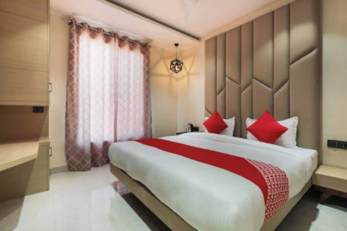 A modern hotel room with a large bed, a nightstand, a wardrobe, and a window with curtains.