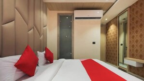 Habitación de hotel con cama, almohadas rojas, colcha blanca, corredor rojo, aire acondicionado de pared, puerta y espejo.