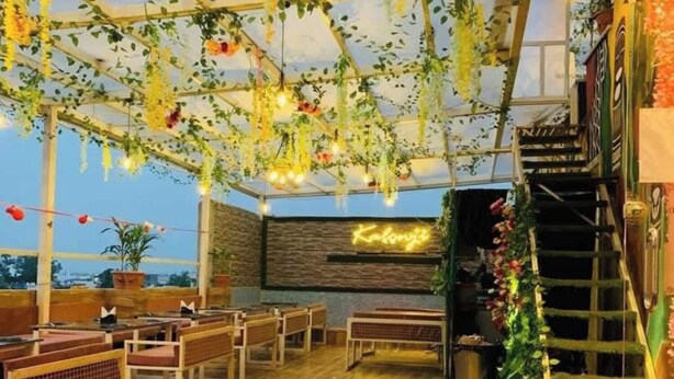 Un espacio interior con bancos de madera, una mesa de vidrio y plantas colgantes.