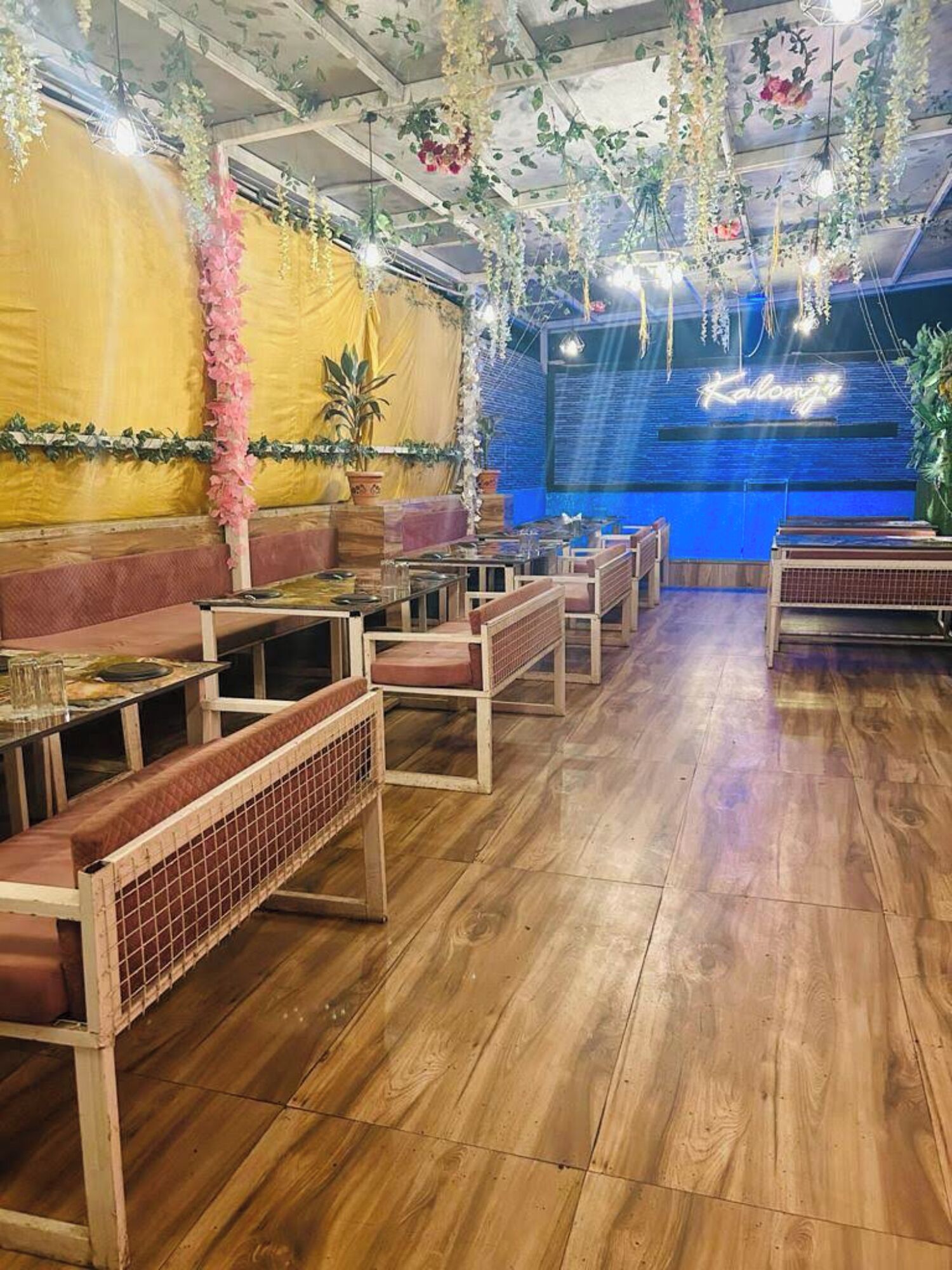 Un restaurante con suelo de madera, bancos acolchados y decoraciones florales colgantes.