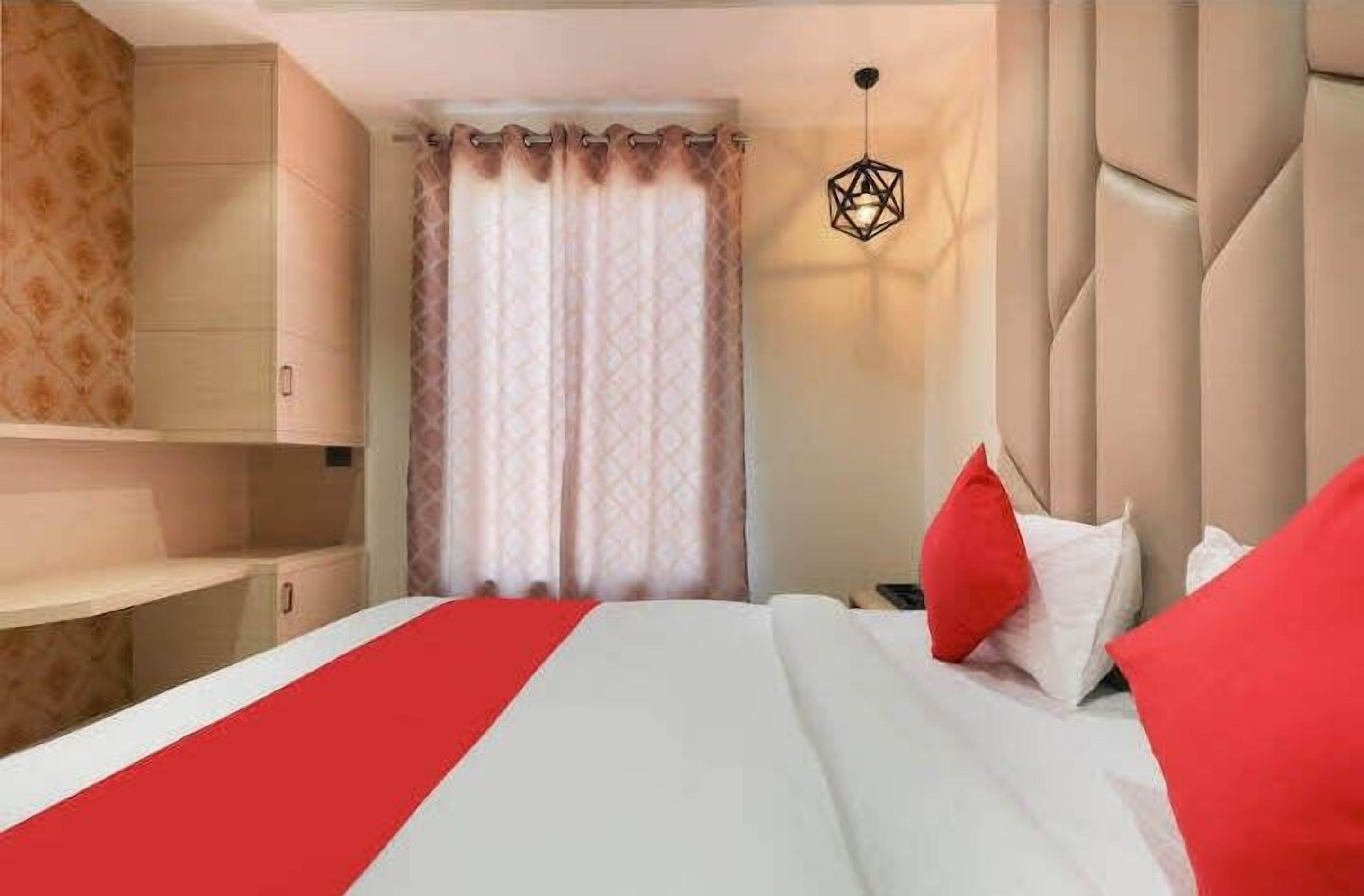 Une chambre d’hôtel comprenant un lit, une armoire, une fenêtre avec des rideaux et un luminaire suspendu.