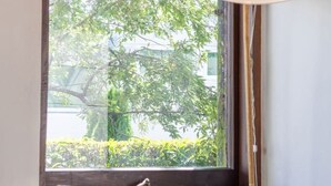 A room with a green sofa, a beige and brown striped pillow, a floor lamp, and a window with a view of greenery outside. - Merivale | King Bed + Carpark, Walk to Hagley Park (Christchurch)